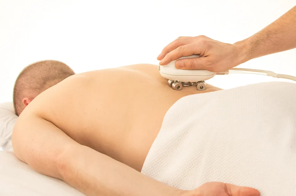 Can You Use a Massage Gun on Stomach? The DOs and DON'ts from our Physical Therapist 5 abdominal muscle ache: a man laying on a massage table while a therapist is passing a device to treat Pain
